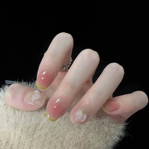 Detail of gradient pink press-on nails with 3D peach charms and yellow French tips