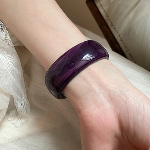 Detail of irregular purple resin cuff bracelet with marbled texture on fabric background