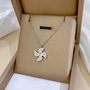 Close-up of silver four-leaf windmill necklace with crystals in a beige jewelry box
