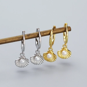Detail of gold and silver shell earrings with pearls hanging on a wooden stand
