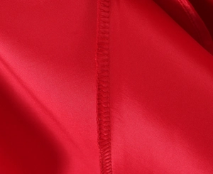 Macro detail of red satin fabric showing high-quality stitching and smooth glossy texture