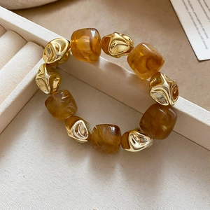 Detail of amber acrylic square beads and irregular golden metal beads on a jewelry box