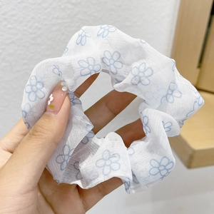 Detail of white mesh hair scrunchie with blue floral pattern held to show texture