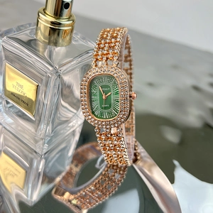 Close-up of gold diamond-set quartz watch with green oval dial on luxury reflective surface