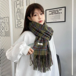 Close-up of soft green plaid scarf with fringe texture and small woven fabric label