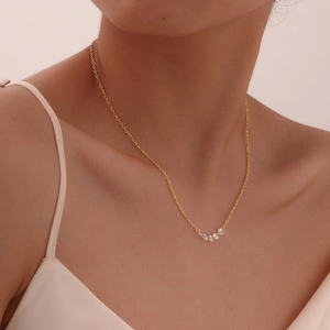 Detail of gold necklace with five white zircons worn on a model's collarbone