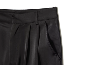 Detail of black satin trousers featuring elegant pleats, waistline and side pockets
