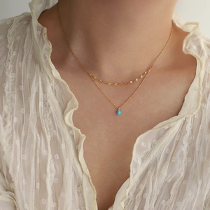 Gros plan d'un collier doré double couche avec pendentif opale bleue en forme de goutte