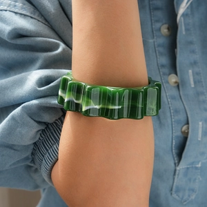 Dettaglio del bracciale in acrilico marmorizzato verde con design a onde su denim