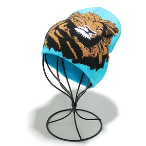 Detail of light blue knit beanie with artistic lion graphic on a display stand