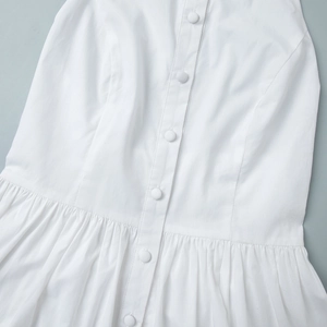 Détail de la robe blanche avec boutons recouverts de tissu et plis à la taille