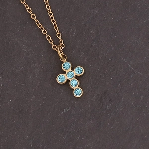 Detail of gold cross pendant necklace featuring six light blue rhinestones on stone background