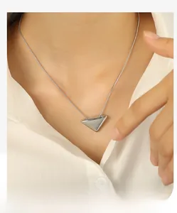 Detailed view of silver triangular pendant necklace on white shirt for women