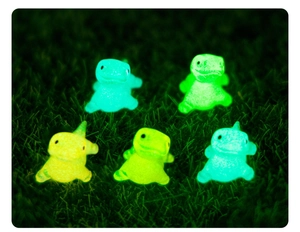 Close-up of five luminous resin miniature dinosaurs glowing green in the dark on grass