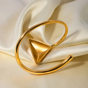Macro shot of 18k gold plated stainless steel triangle bangle on white silk background