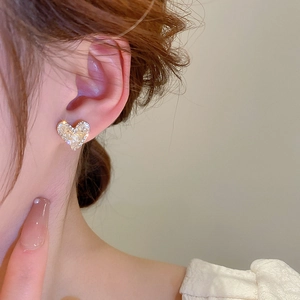 Close-up of heart-shaped gold stud earring with zircon stones on a model ear