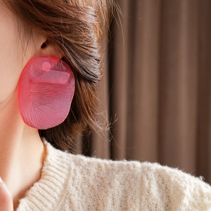 Detail of pink acrylic earring with brushed texture worn by a model in soft light
