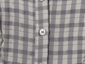 Detailed macro view of grey plaid fabric texture and white four-hole button on the dress