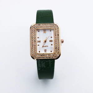 Close-up of square gold watch with crystal bezel and green crocodile leather strap