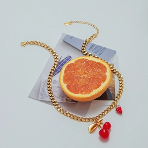 Detail of gold curb chain necklace featuring cherry and strawberry pendants on a magazine