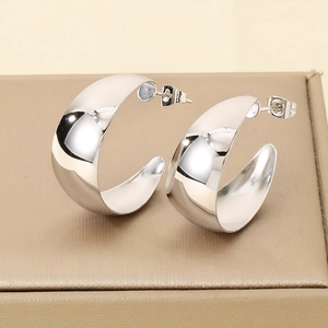 Macro shot of silver C-shaped chunky earrings on a beige jewelry box with glossy metal finish