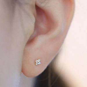 Macro side view of a dainty gold four-leaf clover stud earring with white cubic zirconia