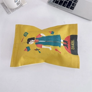 Close-up of a yellow fabric tissue box cover with a cartoon girl illustration on a desk