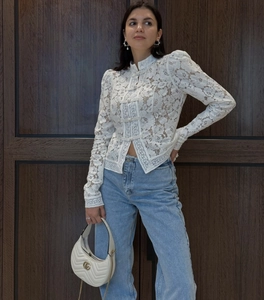 Detalle de una blusa de encaje blanco con cuello alto y mangas abullonadas con vaqueros