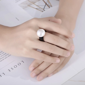 Detail of a large white baroque pearl on a sleek black ring band worn by a model