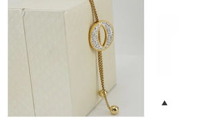 Close-up of golden O-shaped pendant with inlaid crystals on a beaded chain