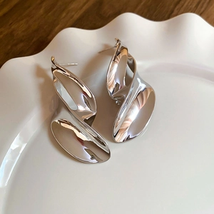 Detailed view of silver irregular twisted metal stud earrings on a textured ceramic plate