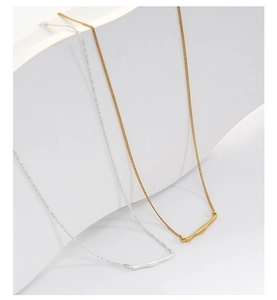 Detail of gold and silver minimalist necklaces with curved bar pendants on white pedestals