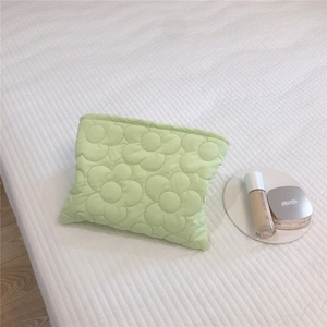 Detailed close-up of mint green quilted floral down pouch on textured white fabric