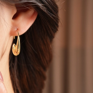 Close-up of a 14k gold plated oval drop earring worn by a model in soft lighting