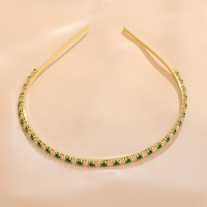 Close-up of golden headband with emerald and white zircon gemstones on silk