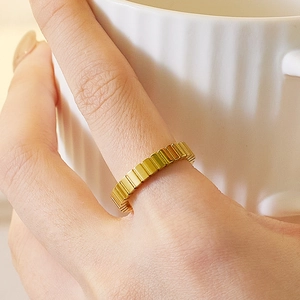 Close-up of gold pleated texture ring on finger holding a white ceramic coffee cup
