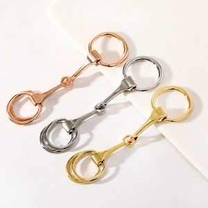 Sleek metal horsebit scarf rings in gold, silver, and rose gold finishes on beige background