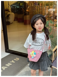 Pink knit crossbody bag with colorful floral charms styled on a child model with denim skirt