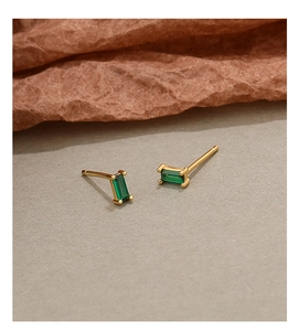 Macro detail of a minimalist gold stud earring featuring a rectangular green zircon stone