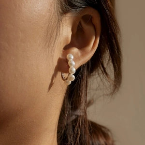 Detailed view of elegant C-shaped silver earrings with five white pearls on model