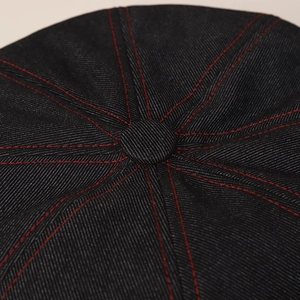 Detail of dark denim beret featuring contrast red stitching and top button structure