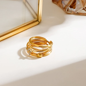 Detail of gold stacked rings with crystal-inlaid cross and heart charms on a white surface