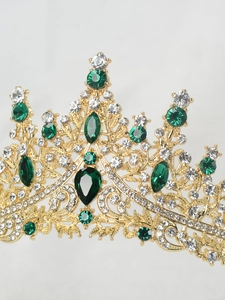 Macro detail of golden princess crown with emerald green and white rhinestones