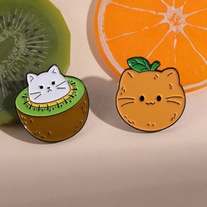 Close-up of cat enamel pins styled as kiwi and orange slices on fresh fruit background
