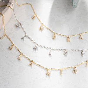 Macro shot of custom stainless steel letter necklaces with zircon pavé on marble