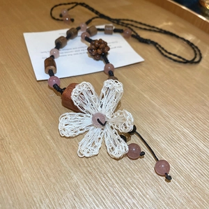 Detail of white woven flower pendant necklace with wood beads on a wooden background