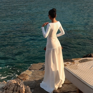 Detailed back view of a white long-sleeve maxi dress with pleats on a coastal beach scene