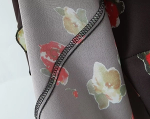 Nahaufnahme von grauem Chiffonstoff mit Blumenmuster und schwarzer Overlock-Nahtkante