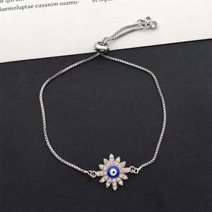 Close-up of a silver sun flower charm bracelet featuring a blue evil eye and box chain