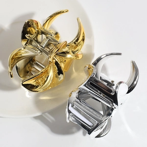 Polished gold and silver metal lily hair claws on a ceramic plate, top-down view